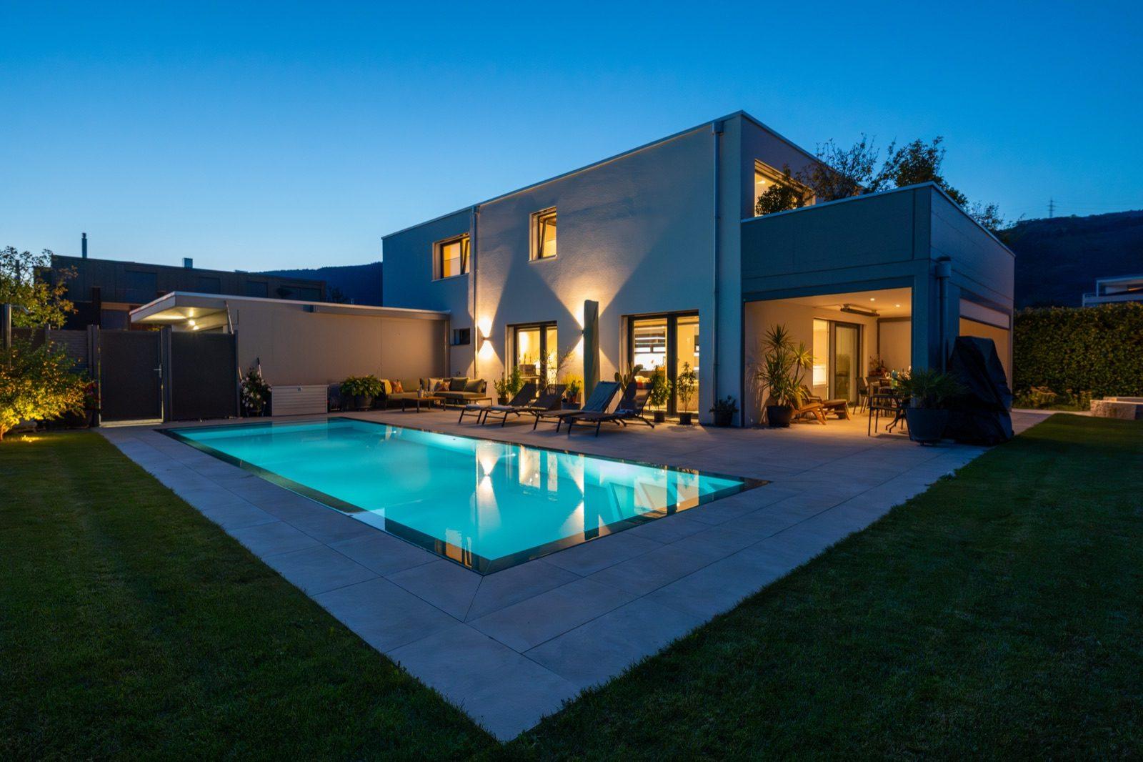 Modernes Wohnhaus mit beleuchtetem Pool bei Nacht